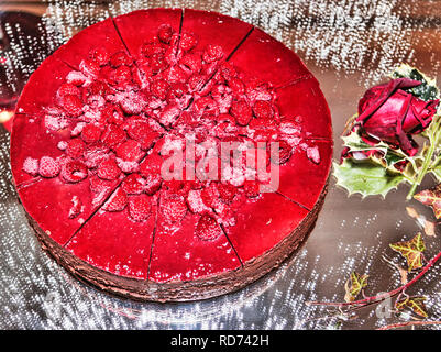 Multi Layer Cake mit Sahne und Himbeeren auf einem Spiegel Schüssel serviert gefüllt mit Puderzucker bestäubt und dekorativen Pflanzen Stockfoto