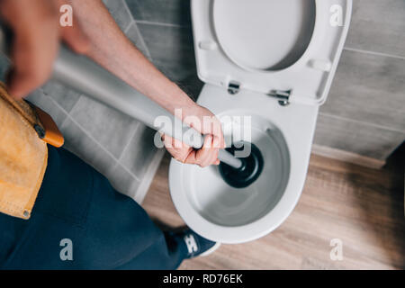 Schuss der männlichen Klempner mit Kolben und Reinigung WC im Badezimmer 7/8 Stockfoto