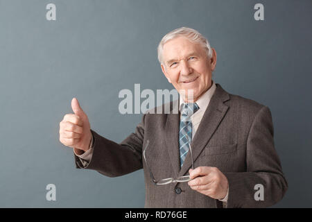 Älterer mann Studio stehen auf grau, Gläser mit Daumen isoliert, positive Stockfoto