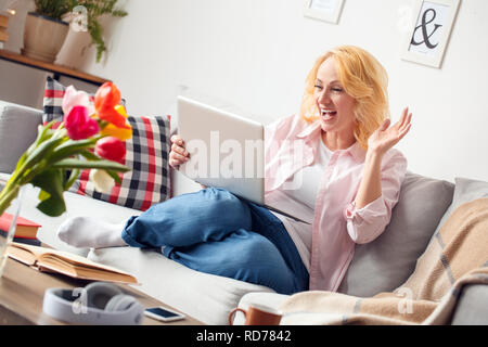 Ältere Frau zu Hause sitzen in Video Anruf auf Laptop lächelt Fröhlich Stockfoto