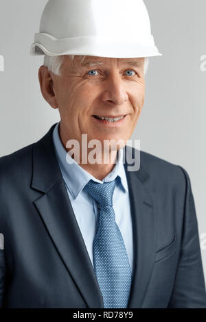 Berufliche Tätigkeit. Konstruktor in harten Hut stehend auf Grau lächelt glücklich in der Nähe isoliert - oben Stockfoto