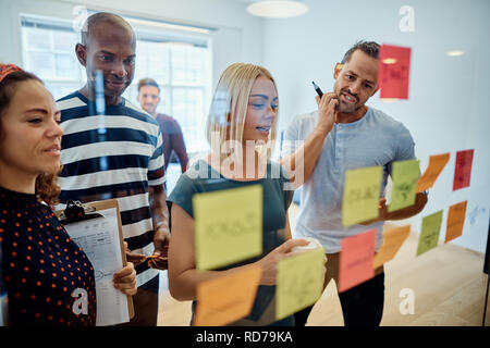 Team von Designern zusammen in einem Büro lesen Haftnotizen auf eine Glaswand Stockfoto