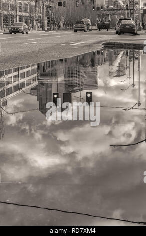 Reflexionen von Seattle Waterfront City Gebäude auf einem großen Regenwasser Pfütze nach einem Wintersturm, der in der Innenstadt von Seattle, Washington, United States. Stockfoto