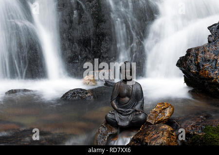 Sitzender Buddha Statue vor einem Wasserfall Stockfoto