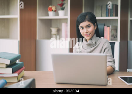 Asiatische junge intelligente Frau Manager mit lässig ihr Geschäft Arbeit mit Laptop und sitzen auf Stuhl in Manager-Zimmer. Stockfoto