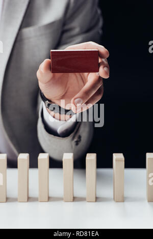 7/8-Ansicht der Mann mit rotem Backstein in Hand mit Holzblöcken im Vordergrund isoliert auf Schwarz Stockfoto