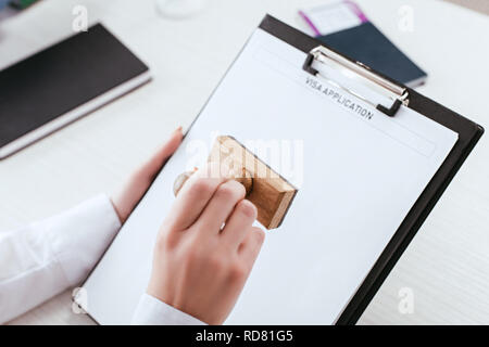 Selektiver Fokus der weiblichen Rechtsanwalt mit Stempel in der Hand, die Zwischenablage mit Visa Application Schriftzüge auf Dokument Stockfoto