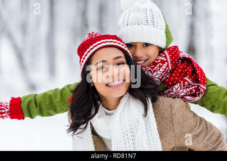 Schöne afrikanische amerikanische Frau huckepack fröhliche Tochter und Kamera in Winter Park Stockfoto