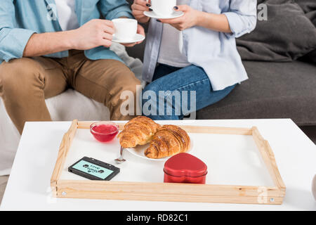 7/8-Ansicht von Paar sitzt auf der Couch und trinkt Kaffee beim Frühstück zu Hause Stockfoto