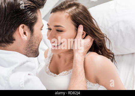 Mann zärtlich berühren Gesicht der Schönen lächelnde Frau im Bett Stockfoto