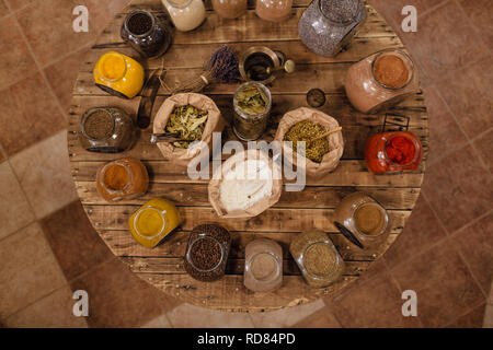 Vielfalt von bunten getrocknete Kräuter und Gewürze auf runden Holztisch in null Abfall Shop angezeigt. Blick von oben auf die Taschen und Gläsern voller Gewürze. Stockfoto