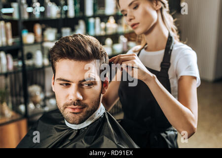 Junge weibliche Friseur Haar kämmen zu stattlichen männlichen Klienten im Beauty Salon Stockfoto