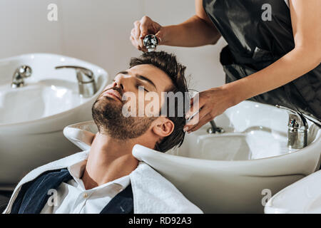 7/8 Schuß von jungen Friseur Haare waschen zu stattlichen Client im Beauty Salon Stockfoto