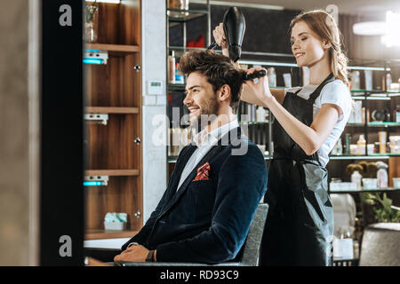 Schöne junge Friseur Haar trocknen zu stattlichen lächelnden Mann im Beauty Salon Stockfoto