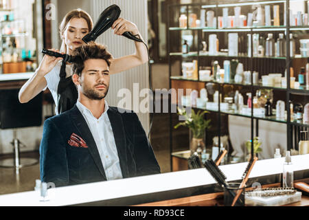 Junge weibliche hairstylist Kämmen und Trocknen der Haare zu stattlichen Client im Beauty Salon Stockfoto