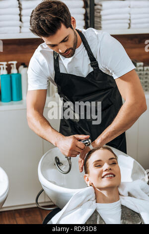 Hübscher junger Friseur Haare waschen lächelnde junge Frau im Beauty Salon Stockfoto