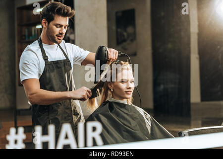 Reflexion im Spiegel der Friseur Haare trocknen zu schöne junge Frau im Beauty Salon Stockfoto