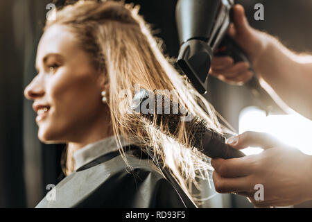 Close-up Teilansicht von hairstylist Kämmen und Trocknen der Haare, schöne junge Frau im Beauty Salon Stockfoto