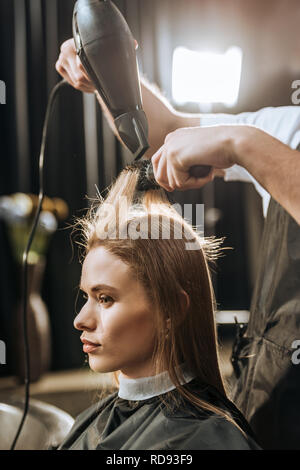 7/8 Schuß von Friseur Haar trocknen, schöne junge Frau im Beauty Salon Stockfoto