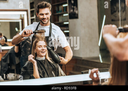 Lächelnden jungen Friseur Haar zu kämmen und trocknen glückliche junge Frau im Beauty Salon Stockfoto