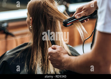 7/8 Schuß von hairstylist Holding Kamm und Haarglätter in einem Schönheitssalon Stockfoto