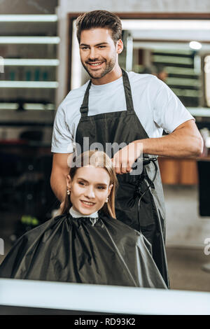 Lächelnd hairstylist mit Haarglätter und glückliches Mädchen an Spiegel im Beauty Salon suchen Stockfoto