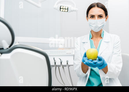 Weibliche Zahnarzt im weißen Mantel und Maske mit Apfel Stockfoto
