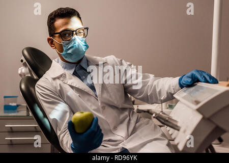 Afrikanische amerikanische Zahnarzt sitzen in Gläsern und Maske und mit Apfel Stockfoto