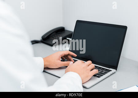 Selektiver Fokus der männlichen Händen der afrikanischen amerikanischen Arzt tippt auf Laptop mit leerer Bildschirm Stockfoto