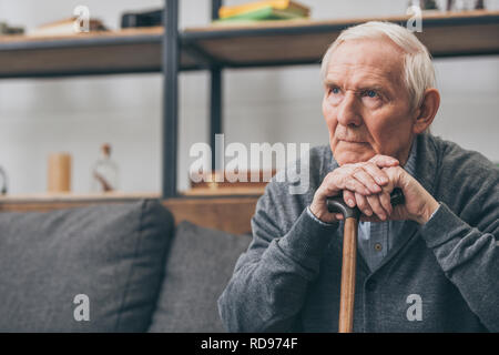 Traurig pensionierter Mann mit grauen Haaren holding Spazierstock im Wohnzimmer Stockfoto