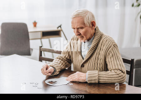 Rentner mit grauen Haaren spielen mit Rätsel zu Hause Stockfoto