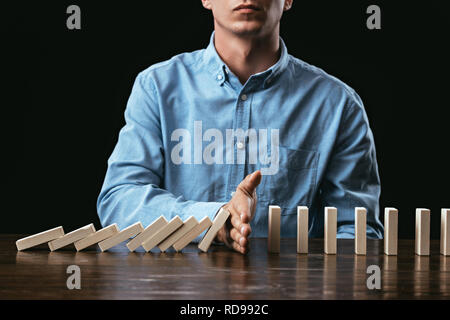 7/8-Ansicht von Mann am Schreibtisch zu sitzen und zu verhindern, Holzklötze fallen. Stockfoto