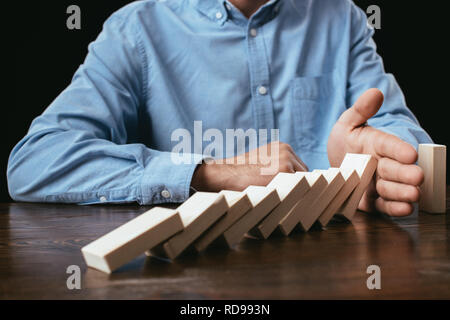 7/8-Ansicht von Mann am Schreibtisch zu sitzen und zu verhindern, Holzklötze fallen. Stockfoto