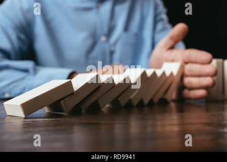 7/8-Ansicht von Mann am Schreibtisch verhindern, Holzklötze von sinkenden mit Hand Stockfoto