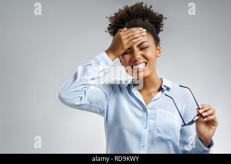 Müde Mädchen leiden unter schmerzhaften Kopfschmerzen und Stress. Foto der afrikanischen amerikanischen Frau in Blau Shirt die Hand auf die Stirn auf grauem Hintergrund. Medi Stockfoto