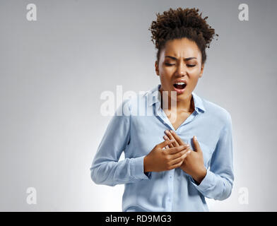 Frau hält die Hände auf schmerzhafte Brust. Foto der afrikanischen amerikanischen Frau in Blau shirt auf grauem Hintergrund. Medizinisches Konzept. Herzinfarkt. Stockfoto