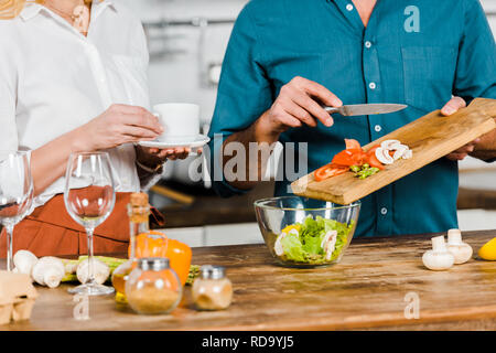 Zugeschnittenes Bild reifer Mann Gemüse in Schüssel und Frau holding Tasse Tee in der Küche Stockfoto