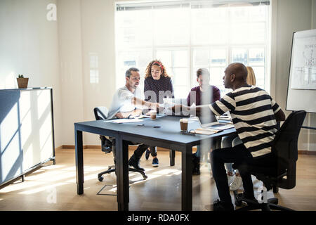 Gruppe von verschiedenen Designern Schreibarbeit diskutieren zusammen sitzen um einen Konferenztisch innerhalb eines Büros Stockfoto