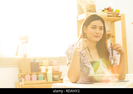 Junge und glückliche asiatische Frau gesund essen Suppe auf dem Tisch in der Küche mit warmem Licht von morgen Sonnenschein mit Kopie Raum Stockfoto