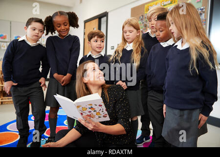 Grundschule Lehrer ein Buch lesen in der Klasse herum drehen auf die Kinder hinter sich stehen zu sehen, Vorderansicht Stockfoto