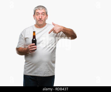 Schöne ältere Menschen trinken Bier Flasche über isolierte Hintergrund mit Überraschung Gesicht zeigenden Finger zu sich selbst Stockfoto