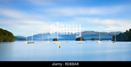 Helle Cool Blue sunrise suchen Lake Windermere durch die Boote in Richtung Ambleside. Lange Belichtung fügt Motion & Reflexion zu Boote und Wolken Stockfoto