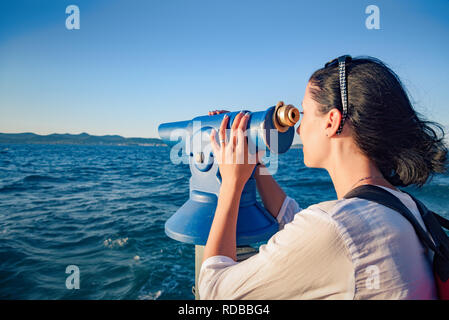 Junge Frau sucht in einem Teleskop oder Fernglas durch das Meer. Stockfoto