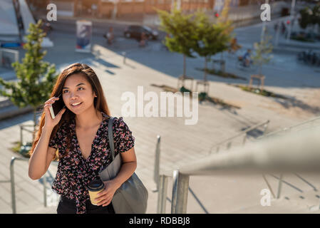 Lächelnd asiatische Studenten Wandern auf dem Campus im Gespräch über Ihr Mobiltelefon Stockfoto