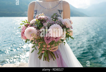 Die Braut hält einen rosa und lila wedding bouquet in ihre Arme vor dem Hintergrund des Meeres Stockfoto
