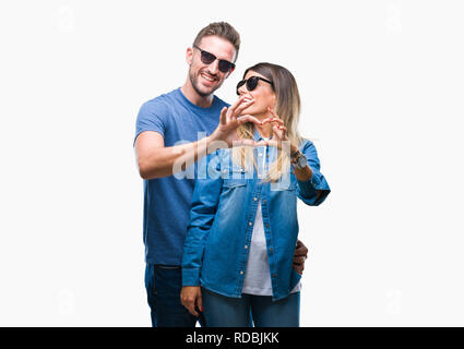 Junges Paar in Liebe Sonnenbrille tragen über isolierte Hintergrund in der Liebe mit Herz und mit Hand lächelnd. Romantische Konzept. Stockfoto