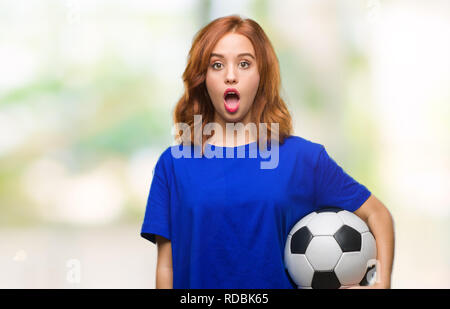 Junge schöne Frau über isolierte Hintergrund holding Fußball Fußball-ball Angst im Schlag mit einer Überraschung konfrontiert, ängstlich und aufgeregt mit Furcht Express Stockfoto