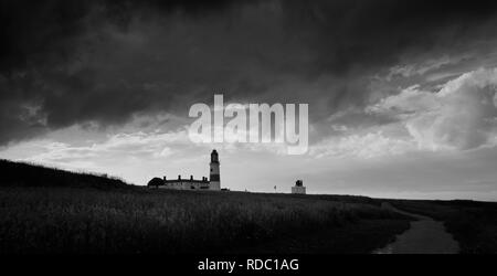 Die schweren Gewitterwolken über der nordöstlichen Küste bedrohen Regen und Sperrung, das Sonnenlicht, das Werfen der Leuchtturm in Silhouette. Stockfoto