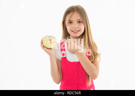 Mädchen mit grossen Lächeln holding Donut. Animierte Dessert, verglaste Bagel mit Augen. Kid zeigen auf süsses, süsses Himmel. Kind mit langem Haar zu tragen rosa Outfit auf weißem Hintergrund. Stockfoto