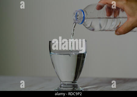 Woman's Hand Trinkwasser Flasche und gießt Wasser in das Glas auf Holz- Tabelle. Stockfoto